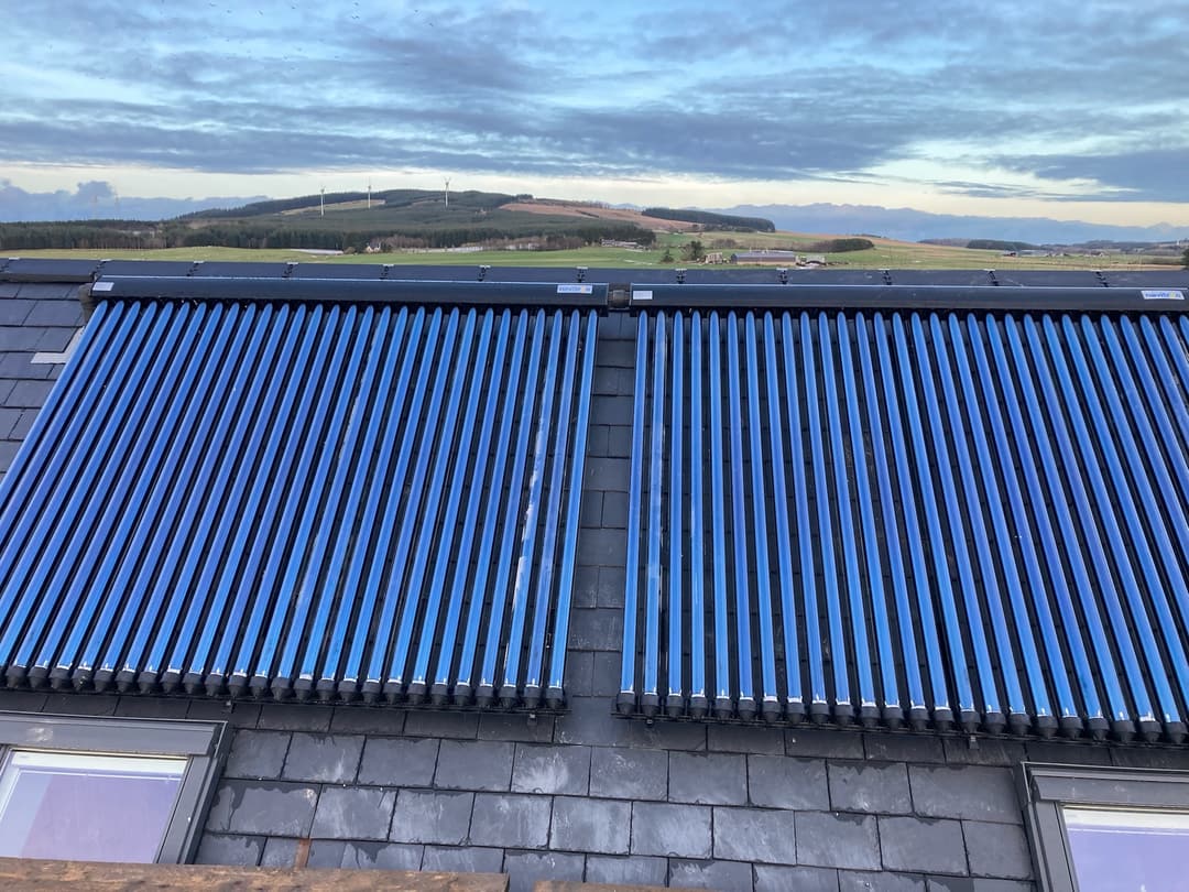 Solar thermal evacuated-tube collectors on a roof with countryside beyond